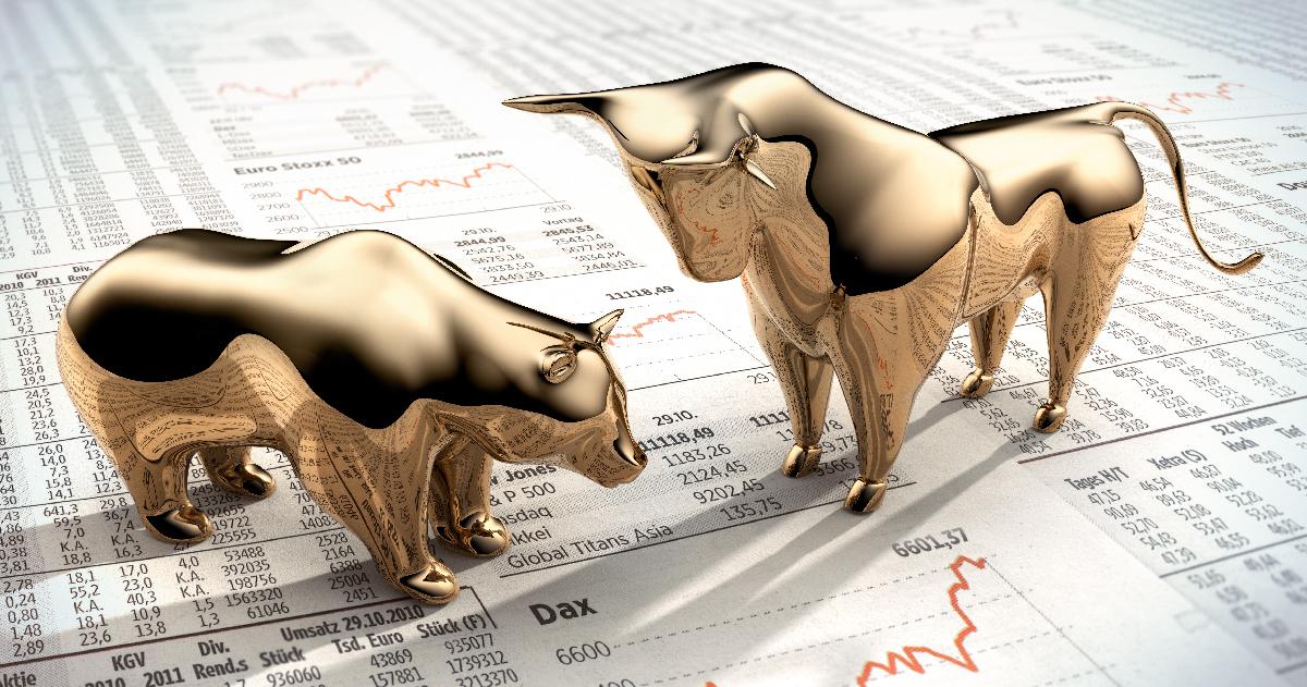 Gold figurines of a bull and a bear standing on top of financial documents 