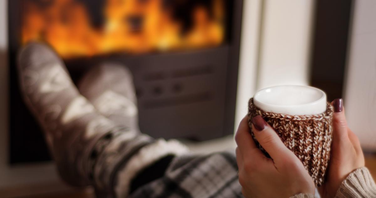 Fireplace with the lower half of a person in pajamas holding a mug.