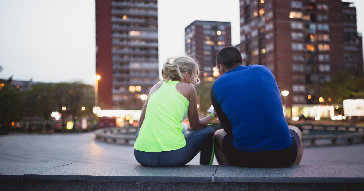 Two people in athletic clothing sit with the city buildings in front of them