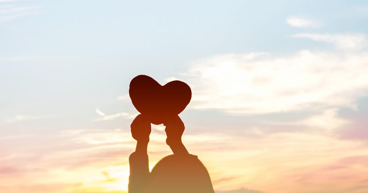 Outline of child holding up a heart shape against the sky