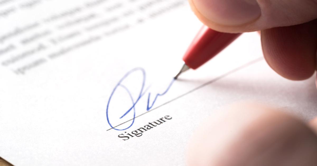 Hand with pen signing legal document