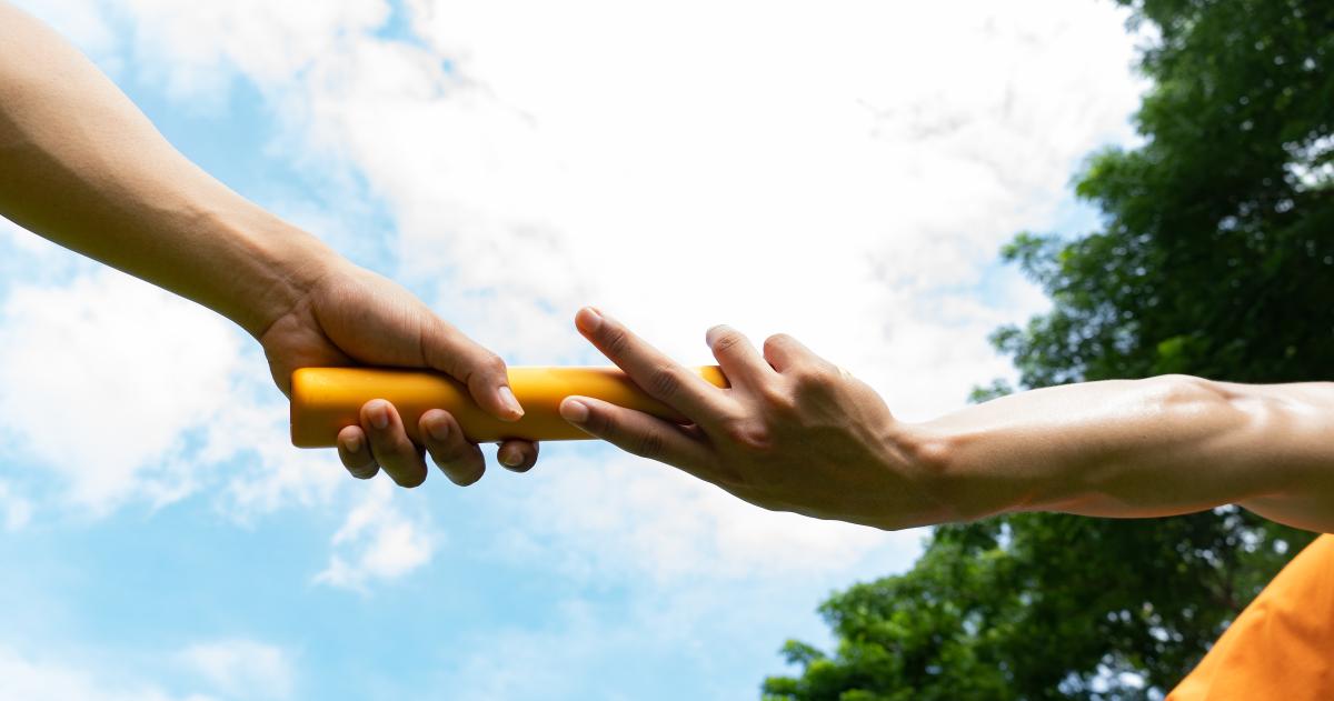 Close up of the hands of two runners passing a metal baton in a relay race