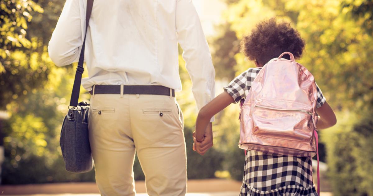 Dad and daughter viewed from behind holding hands, with briefcase and backpack
