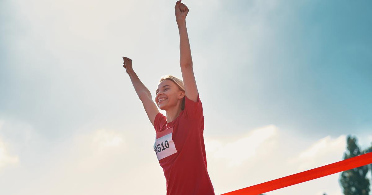 Woman in red running shirt crossing finish line with her arms in the air