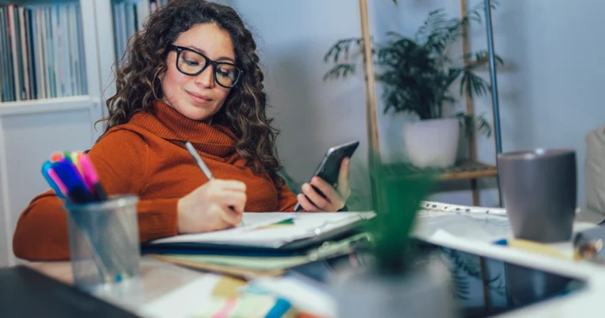 Woman sitting at a desk with a notepad, pencil and phone